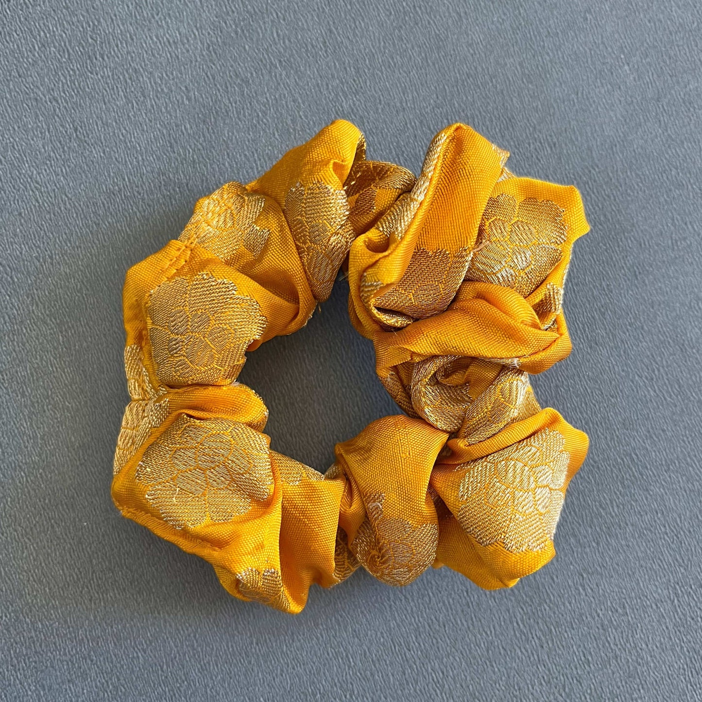 A rich yellow scrunchie with ornate gold patterns, reminiscent of festive or ethnic styles