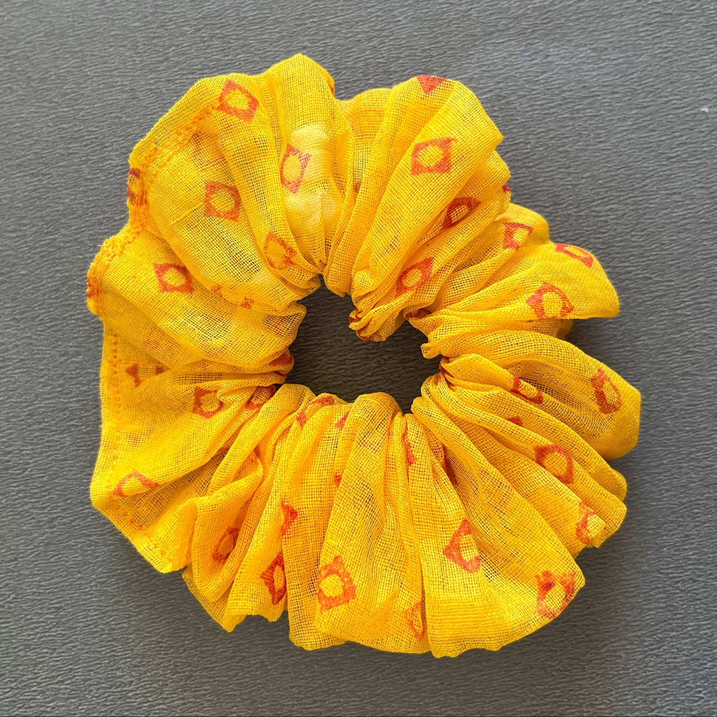 A soft yellow scrunchie patterned with small red/orange geometric accents, perfect for sunny days