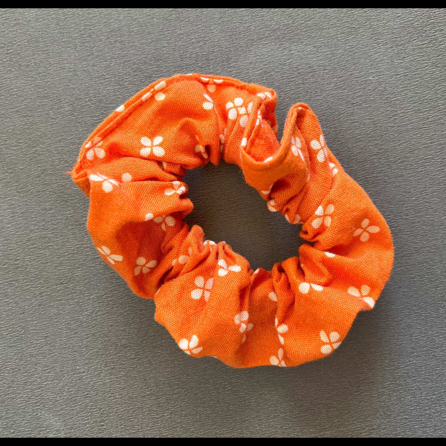 An orange scrunchie dotted with simple white flower motifs, inspired by springtime florals.