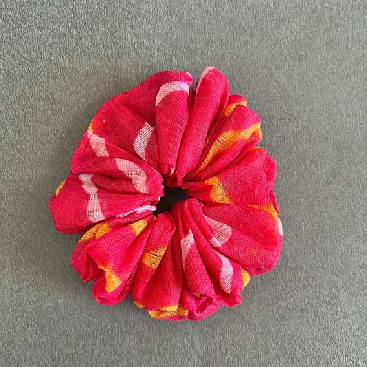 A vibrant red scrunchie with white and yellow tie-dye accents, giving it a lively and youthful appeal