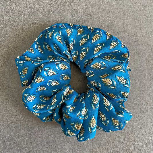 A bold blue scrunchie featuring a delicate gold and white leaf design, great for statement accessorizing.