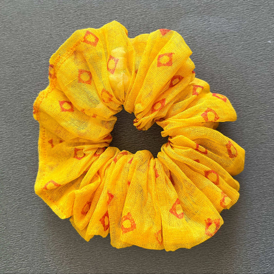 A soft yellow scrunchie patterned with small red/orange geometric accents, perfect for sunny days