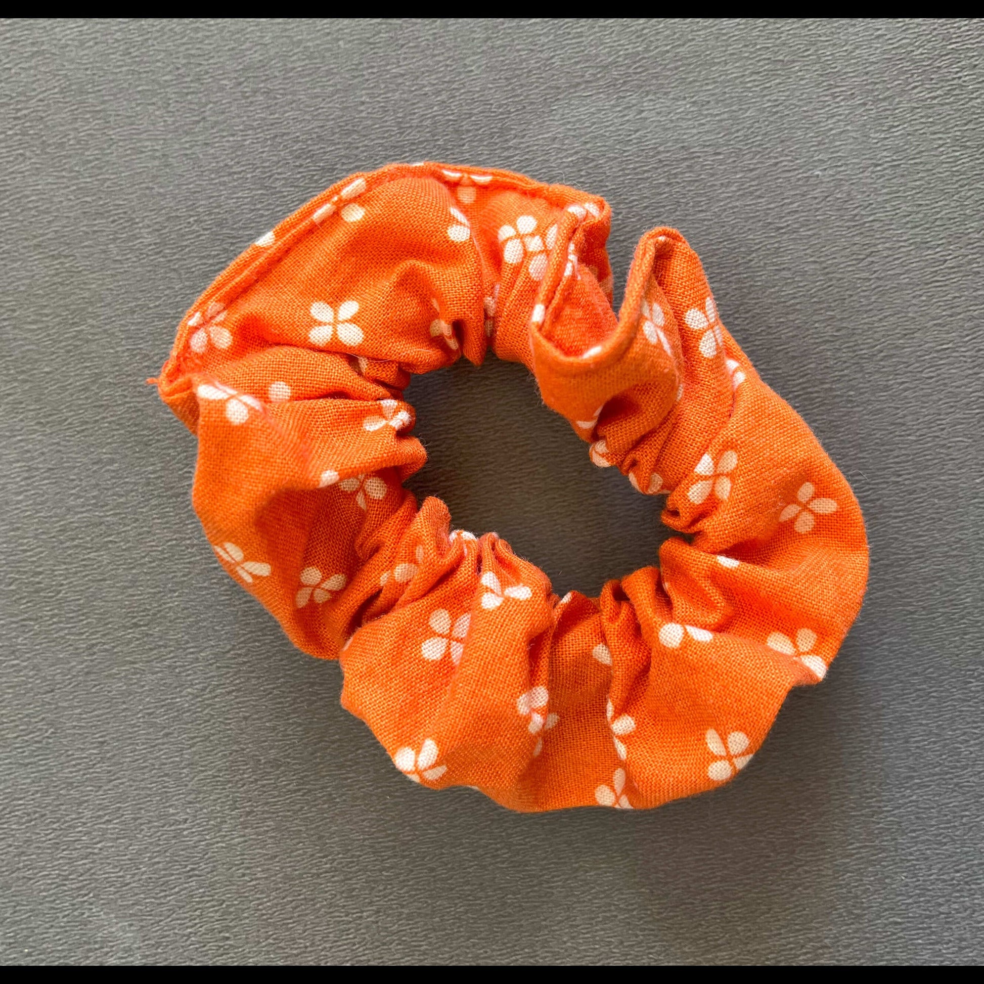An orange scrunchie dotted with simple white flower motifs, inspired by springtime florals.