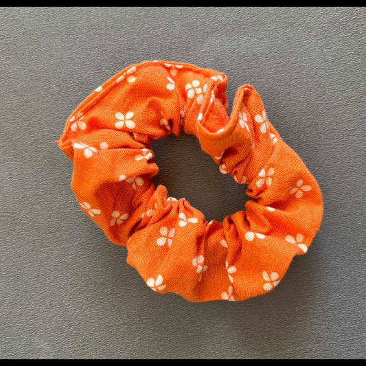 An orange scrunchie dotted with simple white flower motifs, inspired by springtime florals.